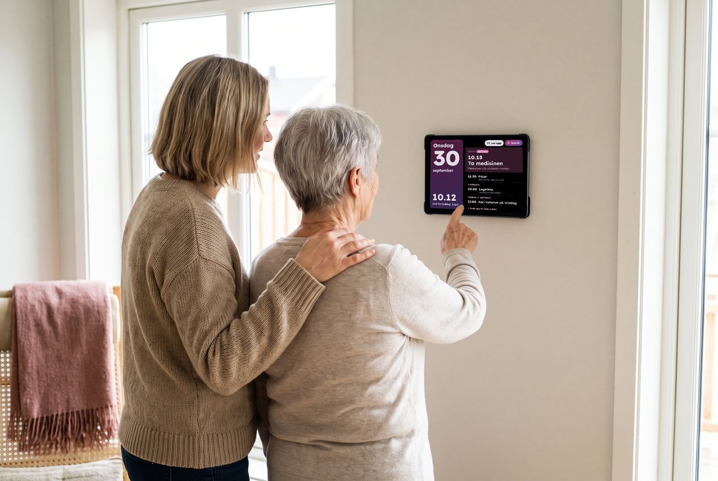 Mor og datter står foran skjermen på veggen. Mor peker på dagens avtaler.